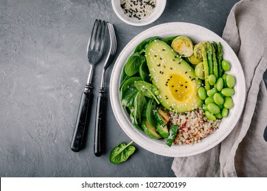 Healthy green vegetarian buddha bowl salad with grilled vegetables and quinoa, spinach, avocado, brussels sprouts, zucchini, asparagus, edamame beans with sesame seeds on dark gray background. 