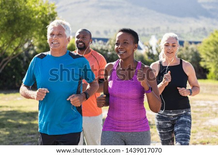 Healthy group of mature people jogging on track at park. Happy senior couple running at park with african friends. Multiethnic middle aged friends exercising together outdoor.
