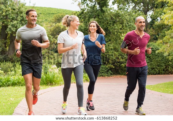 Healthy group of people jogging on\
track in park. Happy couple enjoying friend time at jogging park\
while running. Mature friends running together\
outdoor.