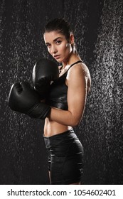 Healthy Gymnastic Woman Kickboxing In Gloves And Standing In Defense Position Under Rain Drops Isolated Over Black Background