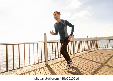 Healthy And Handsome Young Male Model Running On The Beach. The Man Wearing A Mask Is Running By The Sea In Sportswear. Healthy Man Who Does Sports Outside With His Mask Due To Corona Virus Measures.