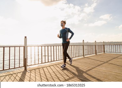 Healthy And Handsome Young Male Model Running On The Beach. The Man Wearing A Mask Is Running By The Sea In Sportswear. Healthy Man Who Does Sports Outside With His Mask Due To Corona Virus Measures.