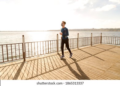 Healthy And Handsome Young Male Model Running On The Beach. The Man Wearing A Mask Is Running By The Sea In Sportswear. Healthy Man Who Does Sports Outside With His Mask Due To Corona Virus Measures.