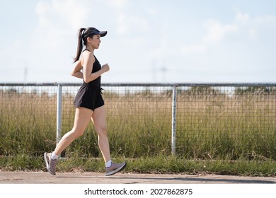 A healthy happy Asian woman runner in black sport outfits jogging in the natural city park under evening sunset - Powered by Shutterstock