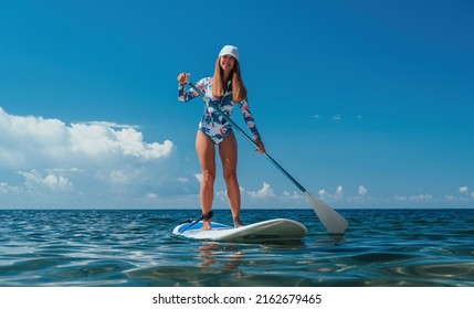 Healthy happy fit woman in bikini relaxing on a sup surfboard, floating on the clear turquoise sea water. Recreational Sports. Stand Up Paddle boarding. Summer fun, holidays travel. Active lifestyle