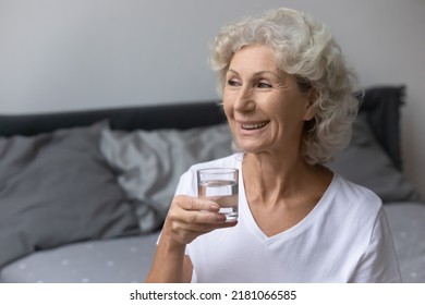 Healthy Happy Mature Woman Starting Morning With Drinking Pure Clean Still Water In Bedroom, Holding Glass, Looking Away, Smiling And Laughing. Elderly Lifestyle, Dehydration, Diet, Healthcare Concept