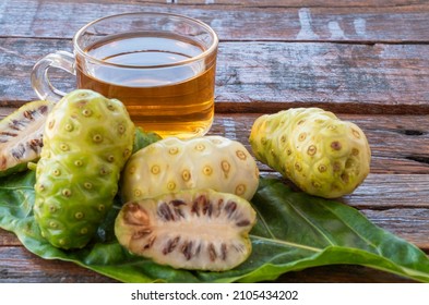 Healthy Herbal Drink In Glass With Fresh Noni Extract, Halved Noni On Green Leaf On Old Wooden Background.