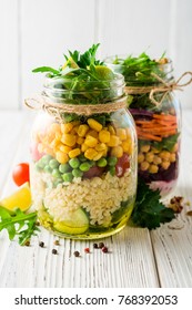 Healthy homemade salads with chickpeas, bulgur and vegetables in mason jars on white wooden background. Selective focus.