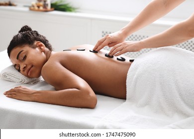Healthy hot stone massage for tranquil black woman at luxury spa salon