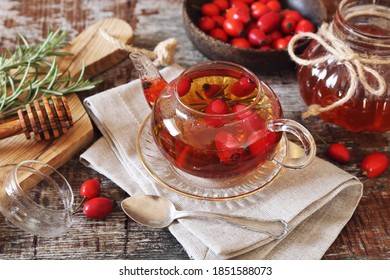 Healthy hot winter beverage. Rose hip tea in teapot, rosemary and berries  on wooden background - Shutterstock ID 1851588073