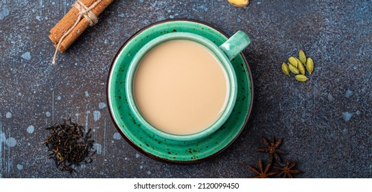 Healthy Indian Beverage Masala Chai - Tea Hot Drink With Milk And Spices In Rustic Green Teacup With Ingredients For Making Masala Chai From Above On Concrete Blue Background