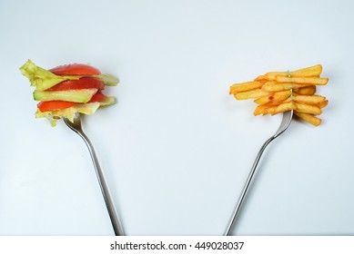 Healthy or junk food choice. Two forks: one with french fries and another with fresh vegetables