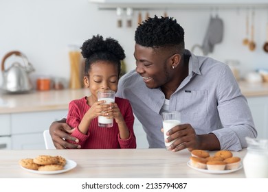 Healthy Kids Lifestyle, Children Nutrition Concept. Cute Little Black Girl Drinking Fresh Milk, Sitting At Table With Her Cheerful Father, Eating Cookies And Cupcakes, Child Spending Time With Her Dad