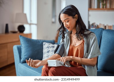 Healthy latin hispanic woman self checking blood pressure using machine. Young mexican woman measuring her own blood pressure with an electronic measurement device at home. Heart rate measurement.