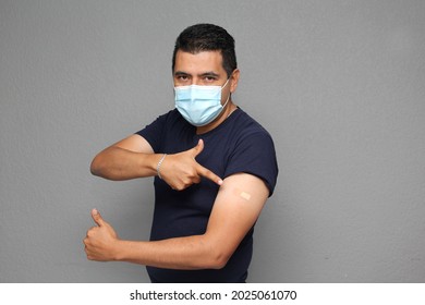 Healthy Latino Adult Man With Mask Showing His Arm That Recently Received The Covid-19 Vaccine
