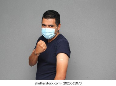 Healthy Latino Adult Man With Mask Showing His Arm That Recently Received The Covid-19 Vaccine
