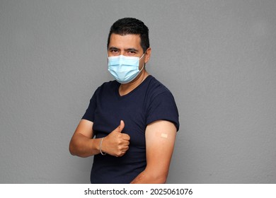 Healthy Latino Adult Man With Mask Showing His Arm That Recently Received The Covid-19 Vaccine
