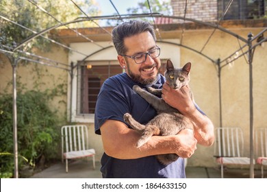 Healthy Latino Man Living With HIV Holding A Gray Cat Outside His Home