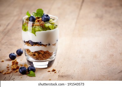 Healthy Layered Dessert With Cream, Muesli, Kiwi And Blueberries On Wooden Background With Space For Text