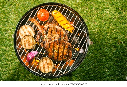 Healthy Lean Pork Loin Cutlets With Assorted Fresh Veggies Grilling Over The Glowing Coals On A BBQ Outdoors On The Green Lawn In A Summer Garden, Overhead View