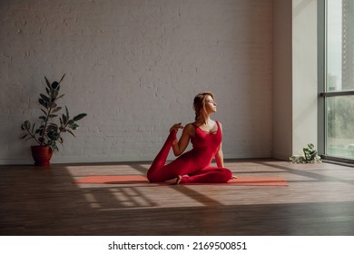 Healthy life style. Young woman in red sports overalls stretches her legs in light yoga studio. Stretching time