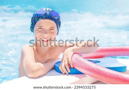 Healthy lifestyle. Active eleven years old child (boy) in cap, sport goggles ready to learns professional swimming with pool board and swim noodles in swimming pool. Caucasian kid enjoying water. 