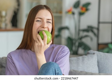 Healthy lifestyle concept. Beautiful young Caucasian woman biting fresh green apple sitting on the couch at home, looking at the camera - Shutterstock ID 2218467447