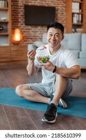 Healthy Lifestyle Concept. Happy Middle Aged Asian Man Eating Fresh Vegetable Salad, Sitting On Yoga Mat After Home Workout And Smiling At Camera. Mature Male Keeping Weight Loss Diet