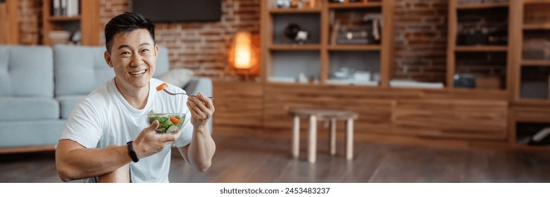 Healthy lifestyle concept. Happy middle aged asian man eating fresh vegetable salad after home workout and smiling at camera. Mature male keeping weight loss diet, panorama with copy space - Powered by Shutterstock