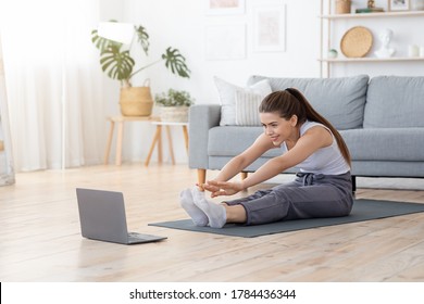 Healthy lifestyle during lockdowm. Flexible girl stretching her body at home, watching videos online on laptop, copy space