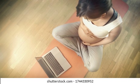 Healthy lifestyle during pregnancy, exercising at home online with laptop during coronavirus, beautiful ambient light and flowers at sunrise / sunset. Prenatal exercises and birth preparation clases.