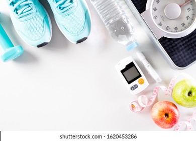 Healthy Lifestyle, Food And Sport Concept. Top View Of Diabetes Tester Set With Athlete's Equipment Weight Scale Measuring Tape Green Dumbbell, Sport Water Bottles, Fruit On White Background.