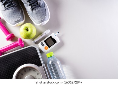 Healthy Lifestyle, Food And Sport Concept. Top View Of Diabetes Tester Set With Athlete's Equipment Weight Scale Measuring Tape Pink Dumbbell, Sport Water Bottles, Fruit On Gray Background.