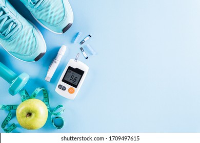 Healthy lifestyle, food and sport concept. Top view of diabetes tester set with athlete's equipment; measuring tape, green dumbbell and  fruit on bright blue pastel background.