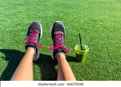 Healthy lifestyle runner girl running shoes selfie with green smoothie. Fitness woman drinking juice to go after workout in park. Healthy lifestyle sporty female athlete POV mobile phone feet picture.