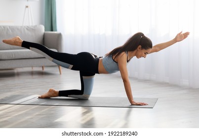 Healthy lifestyle, sport, fitness concept. Young woman in sportswear doing morning yoga at home, standing on fitness mat and stretching her legs and arms, side view, copy space - Powered by Shutterstock