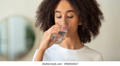 Healthy lifestyle, useful nutrition, diet and water balance for skin at home. Millennial african american lady drinking water from glass in interior of living room, cropped, panorama, copy space