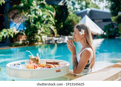 Healthy lifestyle and vacation in Thailand. Portrait of a caucasian young woman which drinks juice swimming in a pool with floating table.