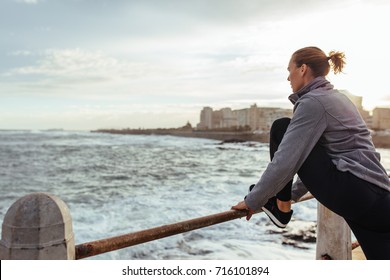 Healthy lifestyle. Woman in sportswear stretching her legs on railing at seaside promenade. - Powered by Shutterstock