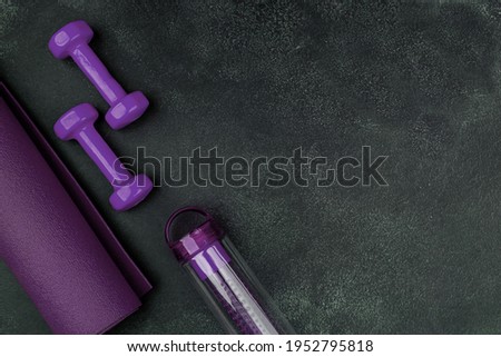 Healthy lifestyle workout concept with training equipment. Purple dumbbells, yogamat and shaker. Black cement background. Empty copy space.