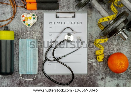 Healthy lifestyle workout concept with training equipment. The idea of how to achieve harmony and longevity while doing sports during Pandemic. Clip board with workout plan tab.