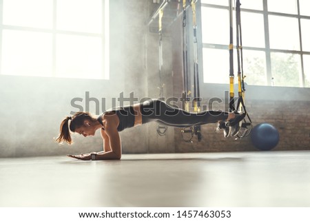 Healthy lifestyle. Young athletic woman doing plank with trx fitness straps in the gym
