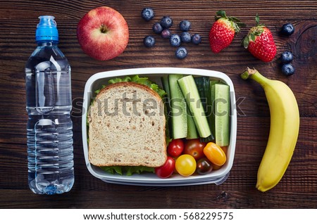 Healthy lunch box with sandwich and fresh vegetables, bottle of water and fruits on wooden background. From top view