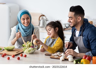 Healthy Lunch. Cheerful Muslim Family Of Three Cooking Vegetarian Meal In Kitchen Together, Happy Middle Eastern Parents And Their Little Daughter Preparing Vegetable Salad, Adding Seasoning, Closeup