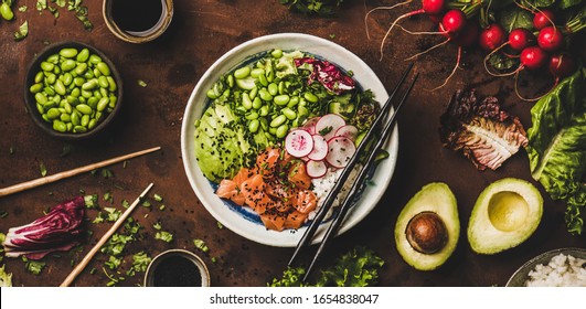 Healthy lunch, dinner. Flat-lay of salmon poke bowl or sushi bowl with vegetables, greens, sushi rice, soy sauce over rusty table background, top view, wide composition. Traditional Hawaiian cuisine
