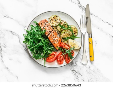 Healthy lunch - roasted salmon, grilled zucchini, arugula tomatoes salad on a light marble background, top view - Powered by Shutterstock