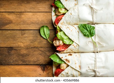 Healthy lunch snack. Tortilla wraps with grilled chicken fillet and fresh vegetables on rustic wooden background. Top view, copy space