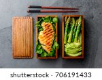 Healthy lunch in wooden japanese bento box. Balanced healthy food grilled chucken and avocado with asparagus and green salad. Top view, slate gray background.