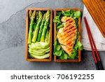 Healthy lunch in wooden japanese bento box. Balanced healthy food grilled chucken and avocado with asparagus and green salad. Top view, slate gray background.