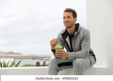 Healthy man drinking green smoothie at home terrace. Sport athlete with spinach cold pressed juice plastic cup drink relaxing outdoors.
